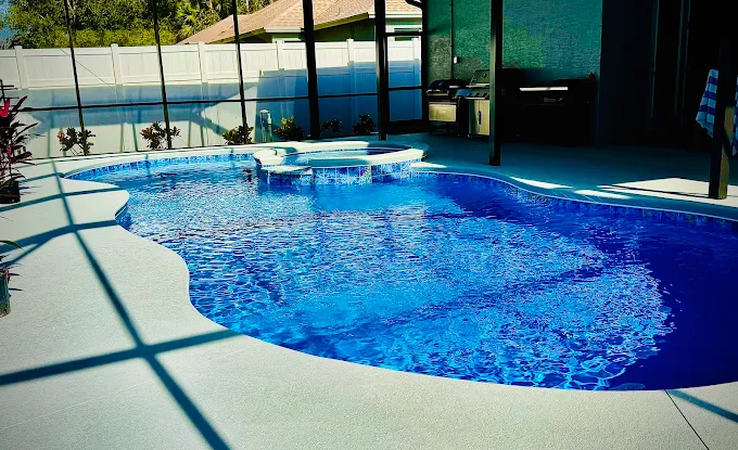 Bright blue in-ground pool with a curved outline and a raised circular spa, under a screened patio with a grill area in the background.