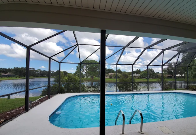 Enclosed backyard pool with blue water, metal screen enclosure, and a lake view beyond.