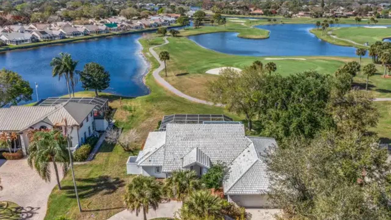 Aerial view of a residential neighborhood beside a winding blue lake and a nearby golf course with green fairways and palm trees.